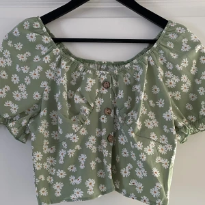 Grön blommig blus från SHEIN - Supersöt ljusgrön blus från SHEIN med prästkrageblommor, puffärmar och knappar framtill. Blusen har offshoulder-modell, smockad rygg och är croppad. Perfekt för dig som gillar romantisk och trendig stil.