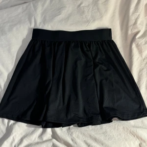 Svart kortkjol från SHEIN - En svart kortkjol från SHEIN i storlek M. Kjolen har en bred resår i midjan och är lätt utställd för en skön och avslappnad look. Tillverkad i mjukt och stretchigt polyestertyg som känns bekvämt hela dagen.