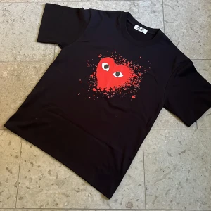 Svart Cdg Play t-shirt - Svart t-shirt från Cdg Play med ett stort rött hjärta med ögon och färgstänk på bröstet. Nytt skick och fraktas inom 24h✅