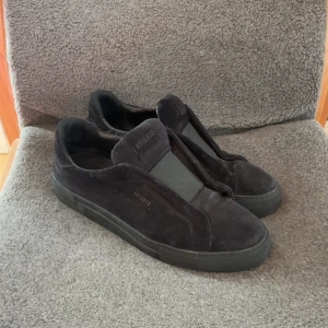 Svarta sneakers från Axel Arigato - Säljer ett par svarta sneakers från Axel Arigato i mocka med stilren design och diskret logga på sidan. Skorna har platt sula och rund tå, och är helt svarta vilket gör dem lätta att matcha. Perfekta för dig som gillar minimalistisk stil. Dustbag tillkommer🤗