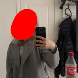 Grå kappa från Vero Moda  - Snygg grå kappa från Vero Moda i storlek XS. Klassisk modell med bred krage och bälte i midjan för en cool siluett. Kappan är fodrad och har långa ärmar, perfekt för höst och vinter. Enkel och stilren design som funkar till många outfits.