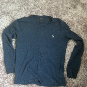 Mörkblå långärmad tröja från Ralph Lauren - Snygg mörkblå långärmad tröja från Ralph Lauren med klassisk rund hals och den ikoniska broderade loggan på bröstet. Tillverkad i mjuk bomull som känns skön mot huden. Perfekt för lager-på-lager och chill vardagsstil. Passar i både M och S