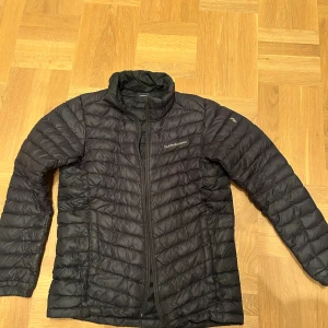 Svart dunjacka Peak Performance 170 - Säljer en svart dunjacka från Peak Performance i storlek 170. Jackan har quiltad design, hög krage och dragkedja framtill. Perfekt för kyliga dagar och riktigt skön att bära. Klassisk och stilren look som funkar till det mesta.
