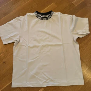 Vit t-shirt från Acne Studios L - Vit t-shirt från Acne Studios med svartvit mönstrad krage och klassisk passform. Tillverkad i en mjuk blandning av viskos, nylon och elastan. Perfekt för dig som gillar stilrena plagg med en twist.