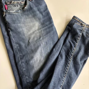 Tramarossa blå jeans med röda detaljer - Snygga blå jeans från Tramarossa med coola röda sömmar på bakfickorna och slitna detaljer vid fickorna. Klassisk femficksmodell med gylf och knapp, samt läderpatch bak i midjan. Jeansen har en rak passform och är tillverkade i mjukt denimtyg. Väldigt fint skick.