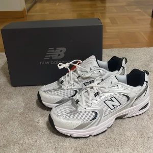 Vita New Balance sneakers med silverdetaljer - Säljer ett par fräscha New Balance sneakers i vitt med silvriga detaljer och svart insida. Skorna har klassisk mesh och syntetmaterial, rund tå och snörning. Perfekta för dig som gillar sportig och clean stil. Boxen ingår.