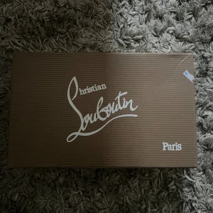 Christian Louboutin svarta sneakers med nitar - Grymma svarta sneakers från Christian Louboutin i mocka med coola svarta nitar på tån och klassisk röd sula. Skorna har snörning och en chunky platt sula. Perfekta för dig som vill sticka ut med en edgy vibe.