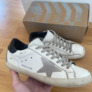 Golden Goose Skor - Golden Goose sneakers i vitt skinn med grå mockadetaljer. Skorna är slitna men i bra skick. Hälarna på sulan har lossnat lätt och sulan på vänster har limmats men billigt att fixa sen. Säg till om du har några frågor!!