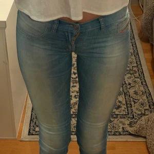 Ljusblå jeans från Diesel - Säljer ett par ljusblå jeans från Diesel med klassisk femficksdesign och väldigt låg midja. Jeansen har snygga slitningar och en tight passform som framhäver benen. Perfekta till sneakers eller boots och passar till många olika stilar.