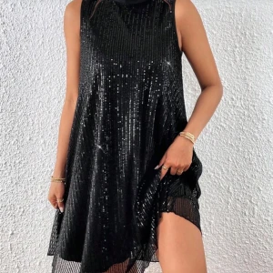 Svart glittrig kort klänning med rosett - Supersnygg svart ärmlös klänning med glittriga paljetter och en stor rosett i nacken. Klänningen är kort och har en lös passform som ger en cool och trendig look. Perfekt för dig som vill sticka ut med lite extra bling.