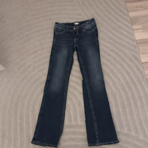 Mörkblå bootcut jeans med broderi - Snygga mörkblå jeans från Gina Tricot med bootcut passform och coola broderade detaljer på bakfickorna. Jeansen har kontrastsömmar, klassisk femficksdesign och dragkedja med knapp. Perfekta för dig som gillar en unik och trendig look.