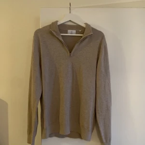 Beige stickad half zip - Snygg beige stickad tröja i storlek M. Tröjan har en stilren krage med half zip och långa ärmar. Perfekt för dig som gillar en enkel och clean look med lite extra detaljer vid halsen. Tröjan är ovannämnd och helt ny utan prislapp. 