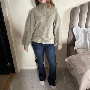 Beige stickad polotröja med ribb - Mysig beige stickad polotröja med bred ribbad kant vid nederdel och ärmslut. Tröjan har en hög krage och en loose passform som ger en chill vibe. Perfekt att slänga på sig när det är kallt ute. Passar dig som gillar enkel och stilren look.