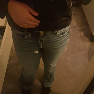 Blå bootcut jeans från Gina Tricot - Säljer ett par blå bootcut jeans från Gina Tricot i storlek 158. Jeansen har snygga strasstenar på bakfickorna som ger extra bling. Klassisk femficksmodell med normal passform och skön stretch i materialet. Perfekta för dig som gillar lite utsvängda ben och coola detaljer.