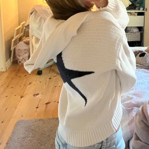 Vit stickad - Vit stickad hoodie med v-ringning och lång ärm. På ryggen finns en stor stjärna. Tröjan har ribbade muddar och en avslappnad, lite loose passform. Perfekt för dig som gillar en chill och trendig stil. I storlek 158/164 men passar Xs och S