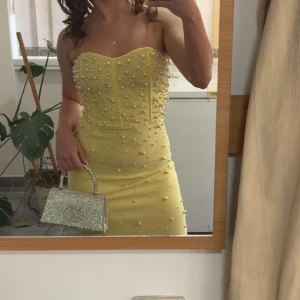Gul axelbandslös långklänning med pärlor - Superfin gul axelbandslös långklänning med figurnära passform. Klänningen har en snygg slits och är dekorerad med massor av pärlor över hela överdelen och nedåt. Perfekt för dig som vill sticka ut med en elegant och unik look. Den är storlek xs med passar s också 