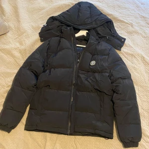 Svart pufferjacka från Trapstar - Svart pufferjacka från Trapstar med avtagbar luva och fet broderad logga på ryggen. Jackan har dragkedja framtill, ribbade muddar och en rund patch med Trapstar-symbol på bröstet. Perfekt för kalla dagar och riktigt snygg streetstil. Sick 9/10 för fler frågor eller bilder så är det bara att slå ett pling. Priset diskuteras vid snabb affär.