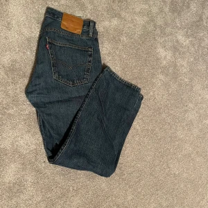 Levi's 501 mörkblå jeans straight fit - Klassiska Levi's 501 jeans i mörkblå tvätt med raka ben och normal passform. Jeansen har fem fickor, knappgylf och den ikoniska läderpatchen bak i midjan. Perfekta för dig som gillar tidlös denimstil.