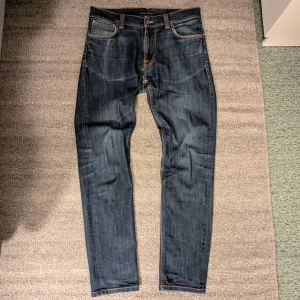 Nudie Jeans - Ett par väldigt fina Nudie Jeans i modellen Thin Finn storlek 32/32. Passformen är slim. De har den klassiska brodyren i vitt på bakfickorna och orangea sömmar. Enda tecken på användning är mindre slitningar i sömmarna till fickorna och i bensluten, samt mindre färgavvikelser efter tvätt. Hör gärna av er om det är något ni undrar över! Mvh Isak