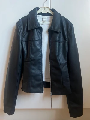 Svart skinnjacka med krage - Snygg svart skinnjacka med klassisk krage och raka linjer. Dragkedja man kan öppna från båda hållen och fickor på sidan som inte syns. Använd en gång, är som ny! Säljer då jag har för många jackor. XS men passar även S. 700 kr från Monki 