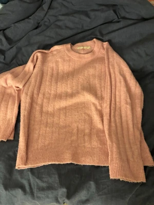 Ljusrosa stickad tröja 157 XS - Mysig ljusrosa stickad tröja från 157 i storlek XS. Tröjan har rund halsringning, ribbade muddar och ett diskret rutmönster i stickningen. Perfekt för lager-på-lager och chill dagar.