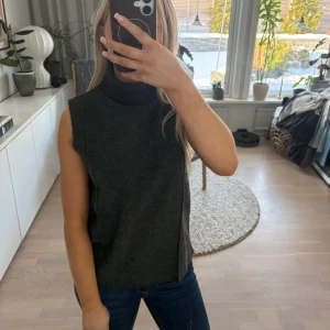 Ärmlös mörkgrå polotröja - Säljer en stilren ärmlös polotröja i mörkgrått. Tröjan har hög krage och rak passform, perfekt att styla över en skjorta eller bära som den är. Materialet är mjukt och bekvämt, vilket gör den enkel att bära hela dagen.