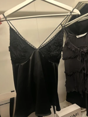 Svart linnetopp från Zara - Snygg svart linnetopp från Zara i nyskick, med tunna axelband och v-ringning. Överdelen har fina spetsdetaljer och resten av toppen är i ett glansigt material som ger en lyxig känsla. Perfekt att styla med jeans eller kjol till festligare tillfällen😍 SKRIV VID FRÅGOR, PRIS KAN DISKUTERAS🙏