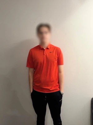 Röd Nike piké stl M - Säljer en röd Nike piké i  Dri-Fit material med klassisk krage och korta ärmar. Tröjan har svart Nike-logga på bröstet och är tillverkad i ett lätt, snabbtorkande syntetmaterial som andas. Perfekt för golfbanan eller sportiga dagar.