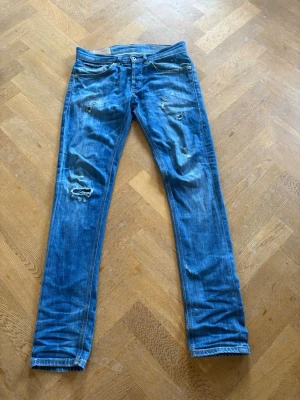 Blå slitna jeans med hål - Säljer ett par blå jeans med slitningar. Jeansen har en klassisk femficksmodell och raka ben. Perfekta för en avslappnad och trendig look. Materialet är denim i bomull och de har en snygg tvättad finish. Priset är inte hugget i sten. 
