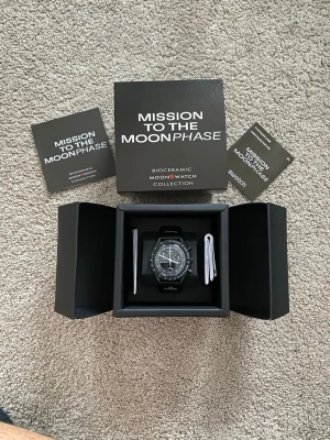 Omega x Swatch MoonSwatch klocka - Snygg svart Omega x Swatch MoonSwatch från Mission to the Moonphase-kollektionen. Klockan har biokeramisk boett, svart urtavla med vita detaljer och tachymeter. Levereras i originalförpackning med manualer.