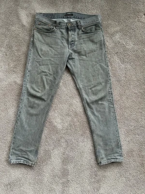 Grå jeans från Nudie Jeans - Snygga grå jeans från Nudie Jeans med klassisk femficksmodell. Jeansen har raka ben och subtila detaljer på bakfickorna. Vid frågor är det bara att slänga iväg ett meddelande!