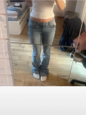 Ljusblå bootcut jeans - Säljer ett par ljusblå bootcut jeans med klassisk femficksdesign och normal midja. Jeansen har utsvängda ben och är tillverkade i denim med en snygg tvätt. Perfekta för dig som gillar en avslappnad och trendig stil.