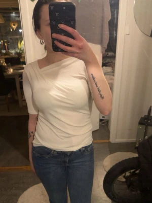 Vit omlottop med oneshoulder - Snygg vit topp med omlottdetalj och oneshoulder-design.