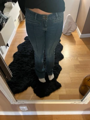 Blå bootcut jeans med brodyr - Säljer ett par blå bootcut jeans med dekorativa sömmar framtill och snygg brodyr på bakfickorna. Jeansen har normal midja och klassisk femficksdesign. Perfekta för dig som gillar en retroinspirerad look och vill ha något som sticker ut lite extra.