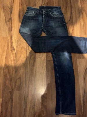 Dondup - Säljer ett par mörkblå jeans med raka ben och snygga slitningar. Klassisk femficksmodell med kontrastsömmar och normal midja. Perfekta till en avslappnad stil och passar till det mesta. Materialet är denim i bomull. W32