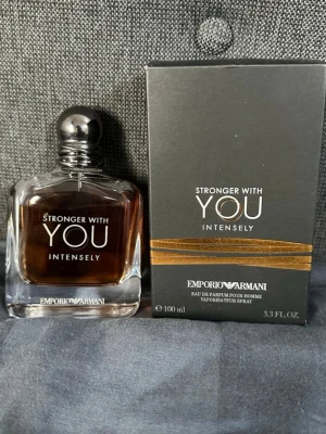 Emporio Armani Stronger With You Intensely - Emporio Armani Stronger With You Intensely är en herrparfym i en elegant glasflaska med mörk bärnstensfärgad vätska och silverfärgad rund kork. Förpackningen är svart med guldiga detaljer och tydlig logga. Flaskan rymmer 100 ml och har en modern, stilren design.