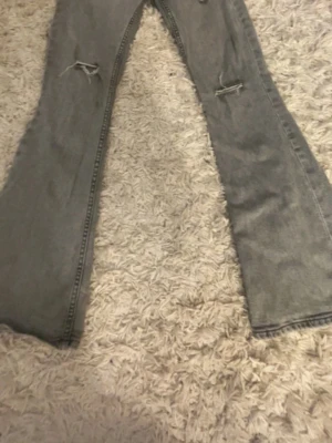 Grå bootcut jeans med slitningar - Säljer ett par grå bootcut jeans med slitna detaljer vid knäna som är gjorda själv. Pris kan diskuteras 