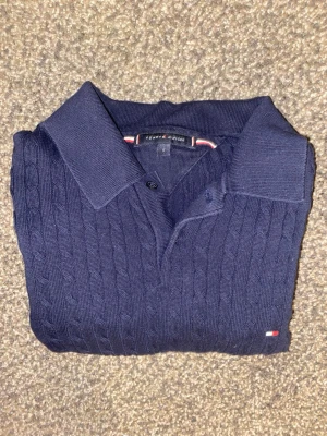 Mörkblå Tommy Hilfiger Piké cable knit - Mörkblå stickad piké från Tommy Hilfiger med kabelstickat mönster. Storlek S. Använd ett flertal gånger, inge defekter, 9/10 skick