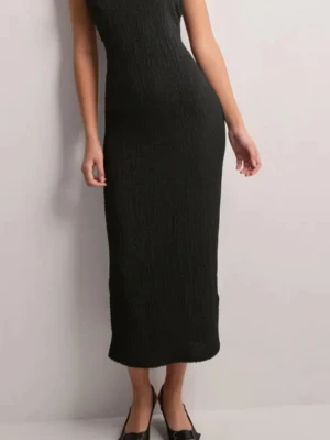 Svart långklänning i ribbad bomull - En stilren svart långklänning med ribbad struktur och ärmlös design. Klänningen har en kroppsnära passform och rund halsringning, perfekt för dig som gillar en enkel men elegant look.