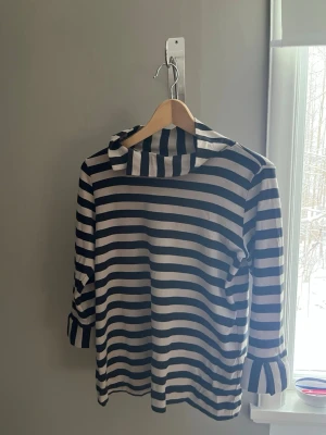 Randig långärmad topp från Jordnära - Säljer en snygg långärmad topp från Jordnära med breda svarta och beiga ränder. Toppen har en lös passform och en bred krage som ger en chill vibe. Perfekt för dig som gillar klassisk stil med en twist. Mkt bra svensk kvalitet och design 100% organisk bomull.