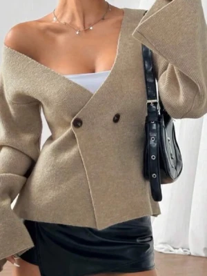 Beige omlott kofta med v-ringning - Säljer en beige omlott kofta med v-ringad design och två knappar framtill. Koftan har långärmade, lite vidare ärmar och är stickad i mjukt material. Snygg offshoulder-look som ger en trendig vibe. Perfekt att styla med linne under.