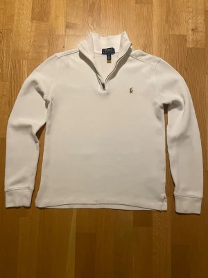 Vit quarter zip tröja från Polo Ralph Lauren - Snygg vit långärmad tröja från Polo Ralph Lauren med klassisk broderad logga på bröstet. Tröjan har en quarter zip-dragkedja vid kragen och är tillverkad i mjuk bomull. Perfekt för chill dagar och enkel att matcha. Finns dock en liten oljefläck vid höger axel, men syns knappt. Prisförslag uppskattas och tveka inte på att fråga!