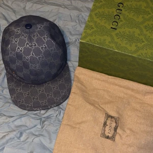 Blå Gucci keps med GG-mönster - Snygg blå keps från Gucci med klassiskt GG-mönster över hela kepsen. Justerbar rem i blått läder baktill och insida i ljus bomull. Kommer med originalbox och dustbag. Perfekt för dig som vill ha en lyxig och trendig accessoar.