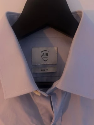 Ljusblå skjorta från SIR of Sweden - Snygg ljusblå skjorta från SIR of Sweden i slim fit-modell. Skjortan har klassisk krage, långa ärmar och knappar hela vägen framtill. Perfekt för dig som gillar stilrena och enkla plagg. Materialet känns mjukt och lätt, troligen bomull. Strl 38 herr