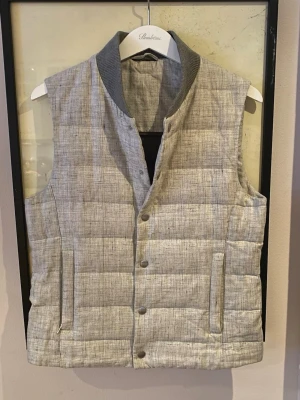 Ljusgrå Quiltad Suitsupply Väst - Snygg ljusgrå väst från Suitsupply i ren linne. Västen har ett quiltat mönster, snygg krage i mörkgrått och fickor på yttersidan och innersidan med dragkedjor, 4 totalt. Stängs med knappar framtill och har en stilren, slim passform. Perfekt för lager-på-lager under kyliga dagar. Storlek Small, passar mig perfekt. Nypris 4499kr