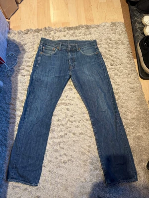 Levi's 501 w31/30 - Klassiska Levi's 501 jeans i blå denim med straight fit och normal passform. Byxorna har fem fickor, knappgylf och det ikoniska läderpatchen bak. Perfekt för dig som gillar tidlös stil och vill ha ett par jeans som funkar till allt.