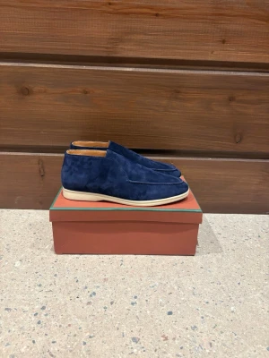 Loro Piana Loafers - Säljer ett par stilrena loafers från Loro Piana i mörkblå mocka med ljus sula och diskret logga bak. Skorna har en klassisk rund tå och är fodrade med ljusbrunt skinn invändigt. Perfekta för dig som gillar lyxiga och bekväma skor med clean look. Pris är diskuterbart! 