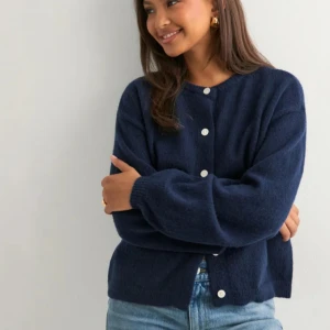 Mörkblå kofta från Nelly - Mysig mörkblå kofta från Nelly med rund halsringning och vita knappar framtill. Koftan är stickad i ett mjukt material.  Nypris 399kr. Fick i julklapp så kan inte returnera. Den är helt oanvänd, endast provad!💕