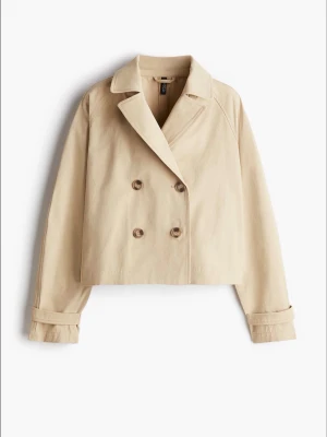 Beige kort trenchcoat med knappar - Snygg beige trenchcoat från H&M med dubbelknäppning och klassisk krage. Jackan är croppad och har långa ärmar med dekorativa detaljer vid mudden. Perfekt för dig som vill ha en stilren och modern look. Knappt använd! Tar emot byten