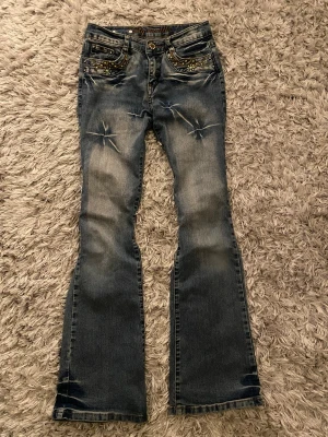 Big Mantis blå bootcut jeans med broderi - Snygga blå jeans från Big Mantis med bootcut passform och coolt broderi i grönt på fickorna. Jeansen har slitningar och mycket detaljer. Materialet är klassisk jeans med tvättad look och broderade mönster både fram och bak.